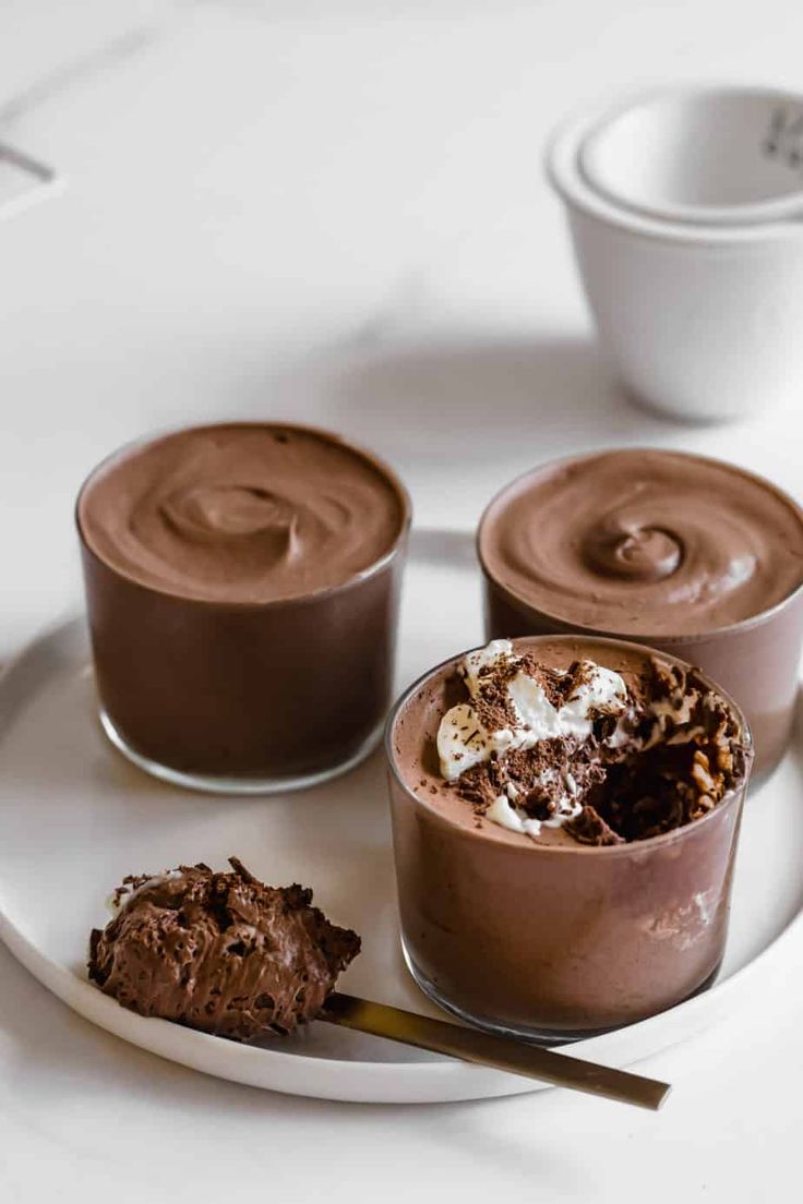 three desserts are sitting on a plate with spoons and cups in the background