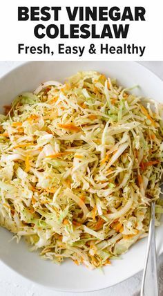 a white bowl filled with coleslaw next to two silver spoons on top of a table