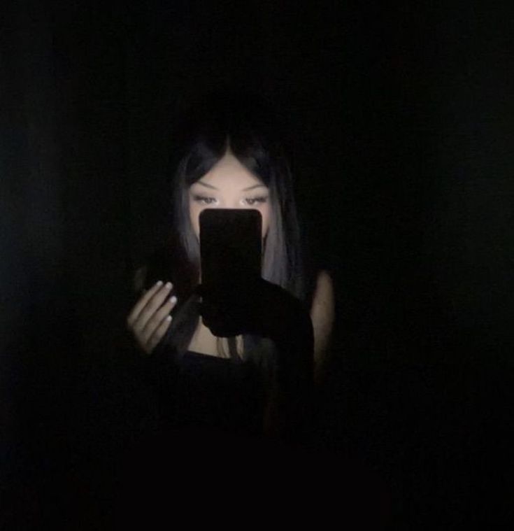 a woman holding a cell phone in front of her face with dark lighting behind her