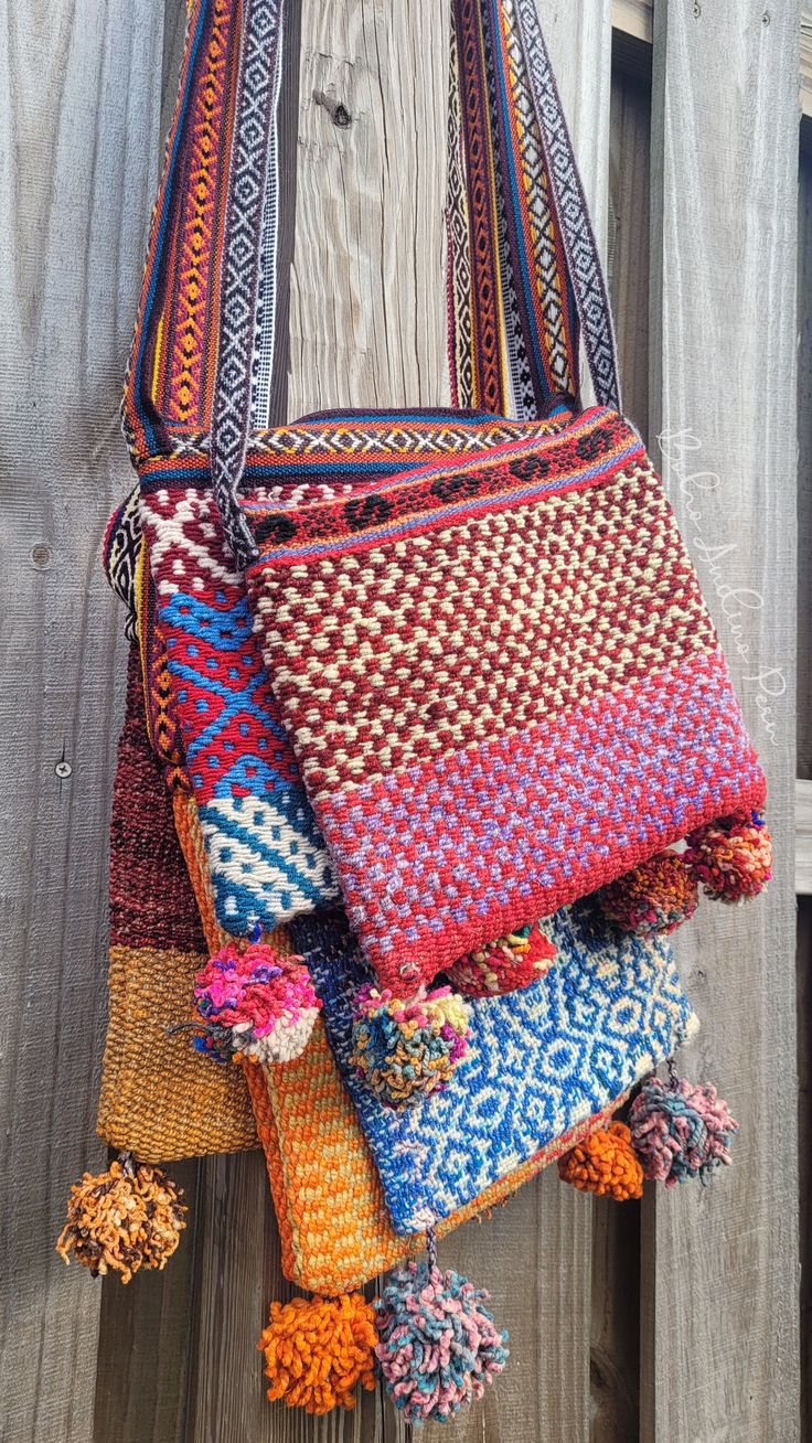 a multicolored bag hanging on a wooden fence with tassels and pom poms