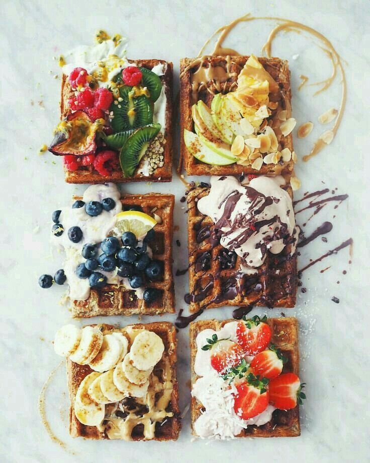 four waffles with fruit and ice cream on them, sitting on a marble surface