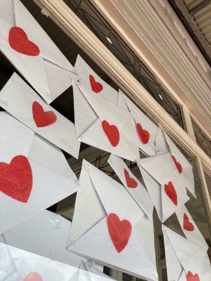 paper hearts are hung from the ceiling in front of a window with red and white envelopes