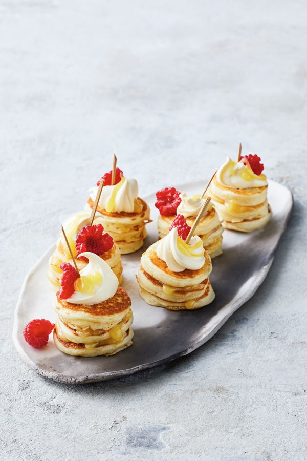 small pancakes topped with whipped cream and raspberries on a silver platter, ready to be eaten