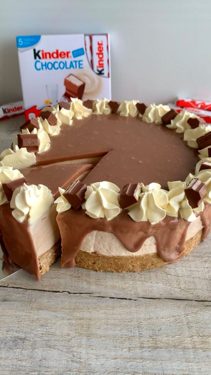 a chocolate cake with white frosting on a wooden table next to a box of kinder chocolate