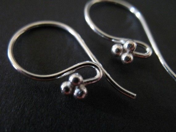 two pairs of silver earrings sitting on top of a black surface