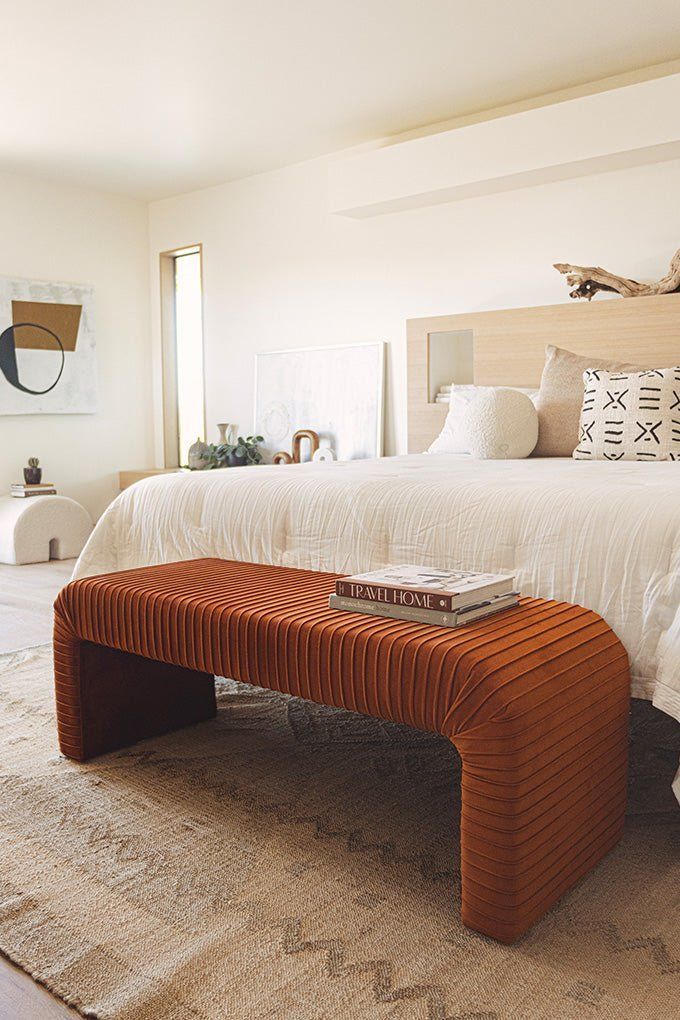 a bedroom with a large bed and an orange bench on the floor in front of it