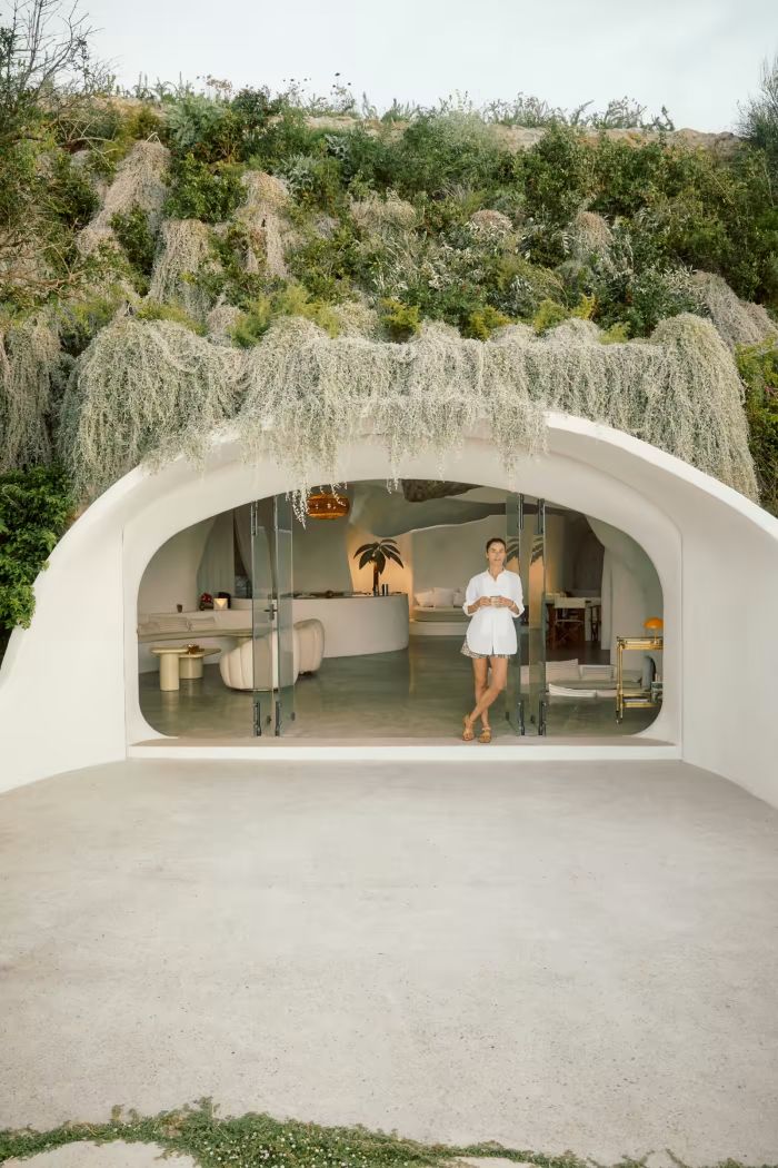 a woman standing in front of a white building with plants growing on the roof and walls