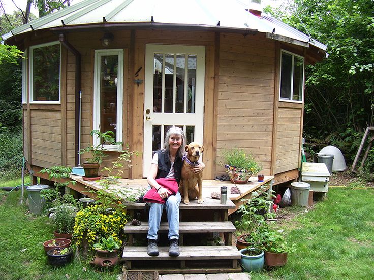 a woman sitting on steps with her dog in front of a tiny cabin style house