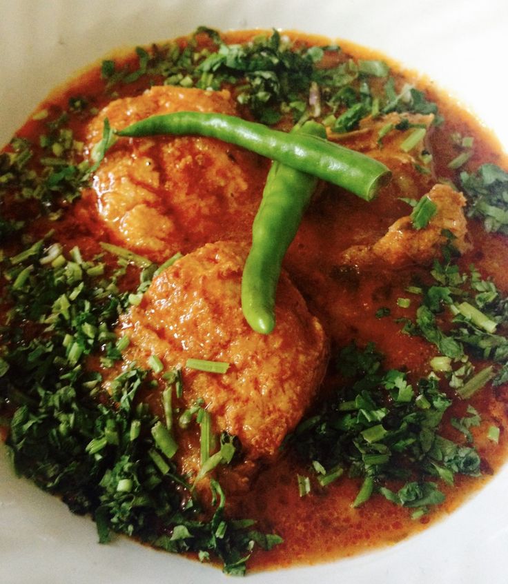 a white plate topped with meat covered in sauce and green vegetables on top of it