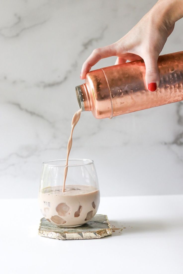 a person pouring something into a glass on top of a white table with marble background