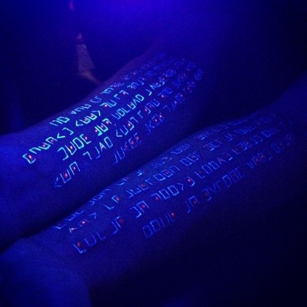 two arm sleeves with writing on them in the dark, lit up by blue light