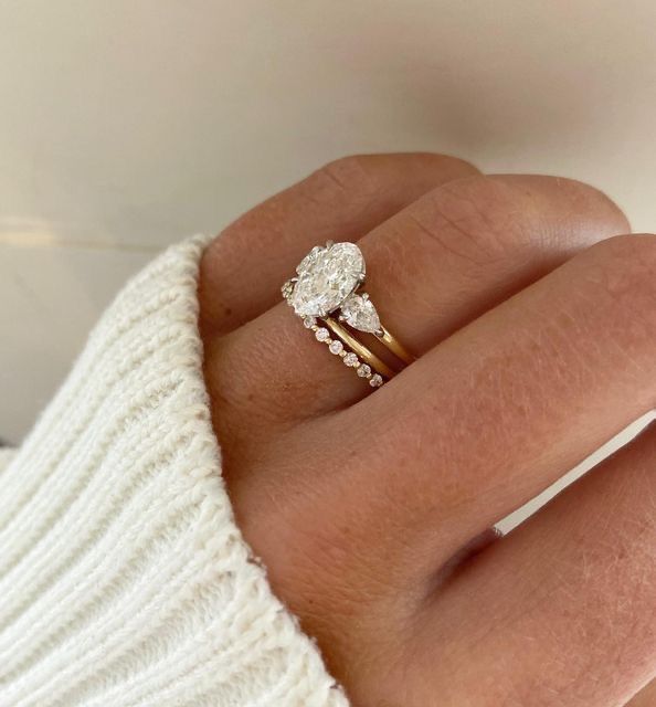 a woman's hand with a diamond ring on top of her finger and a white sweater in the background