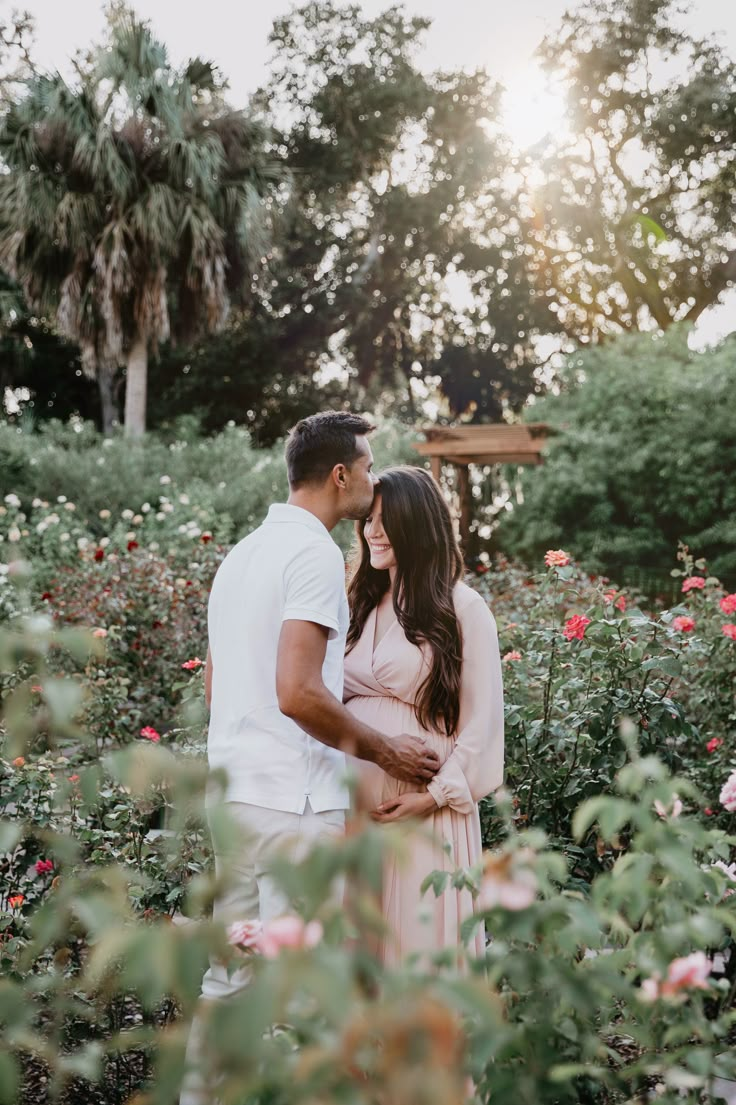 a man and woman are standing in the middle of some flowers with their arms around each other