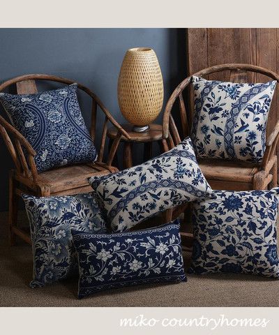 four blue and white pillows sitting on top of a wooden chair next to a vase