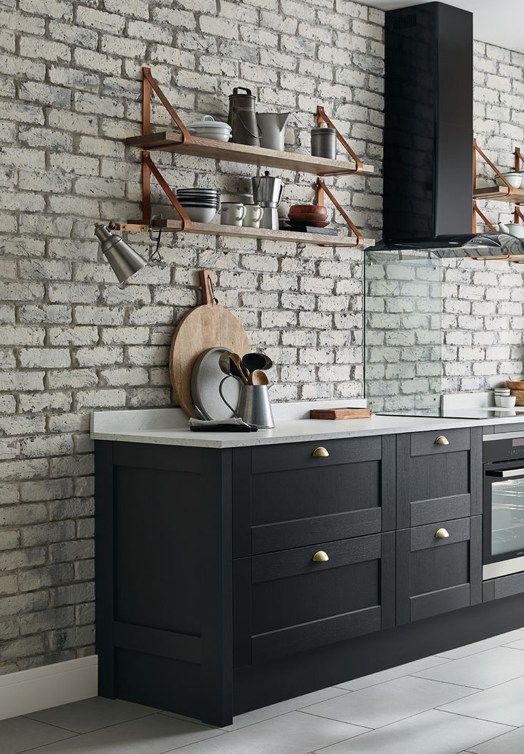 a kitchen with black cabinets and white brick wall behind the countertop, along with open shelving