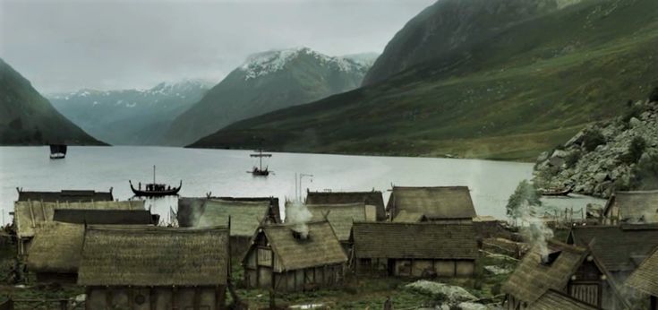 an old village with thatched roofs and mountains in the background, surrounded by water