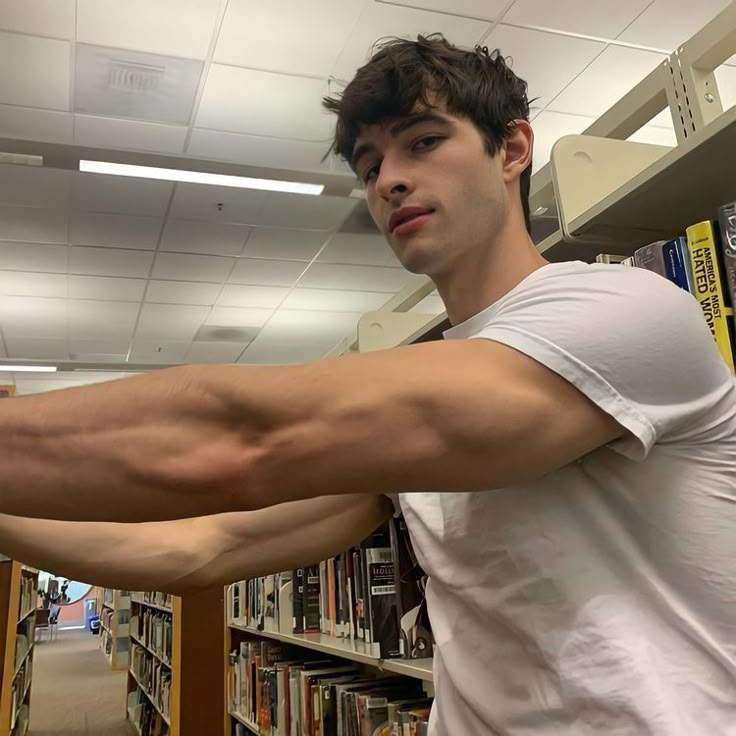 a man with arm muscles standing in front of bookshelves