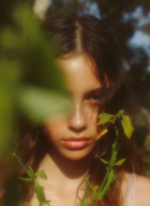 a woman with long brown hair and green leaves around her neck looking at the camera