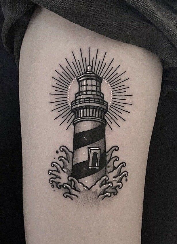 a black and white lighthouse tattoo on the right thigh, with waves around it's base