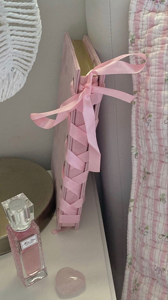 a bottle of perfume sitting on top of a table next to a pink bed sheet