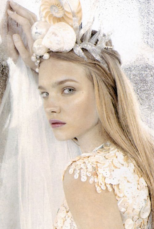 a woman wearing a veil and flowers on her head standing next to another woman in a white dress