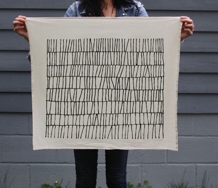 a woman holding up a piece of art with lines drawn on it in front of her