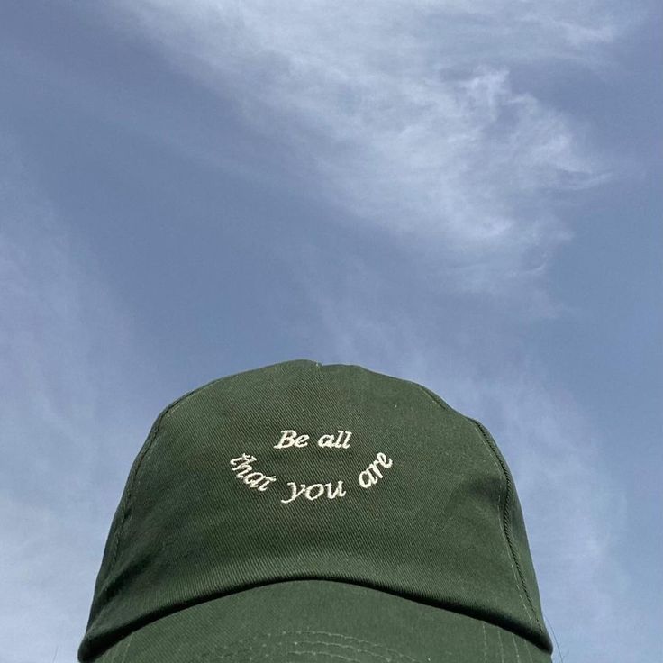 a green hat with the words be all that you can written on it against a blue sky