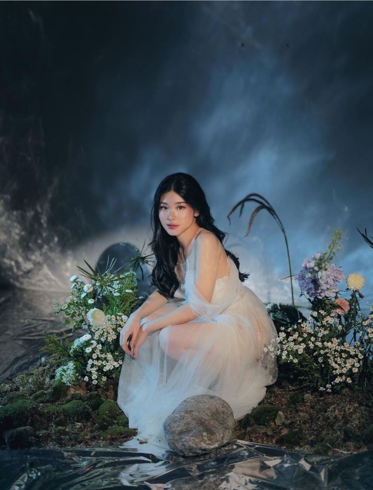 a woman sitting on top of a rock in front of flowers and plants with dark clouds behind her