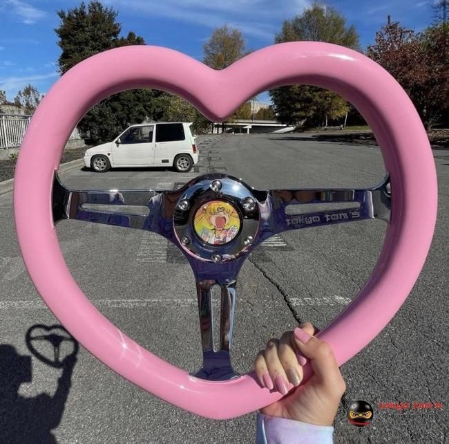 a person holding up a pink heart shaped object in the middle of a parking lot