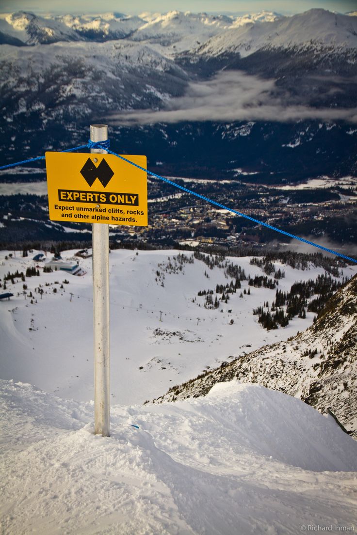 a yellow sign that is on the side of a snow covered hill with mountains in the background