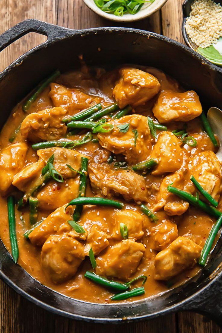 a pan filled with chicken and green beans on top of a wooden table next to other dishes