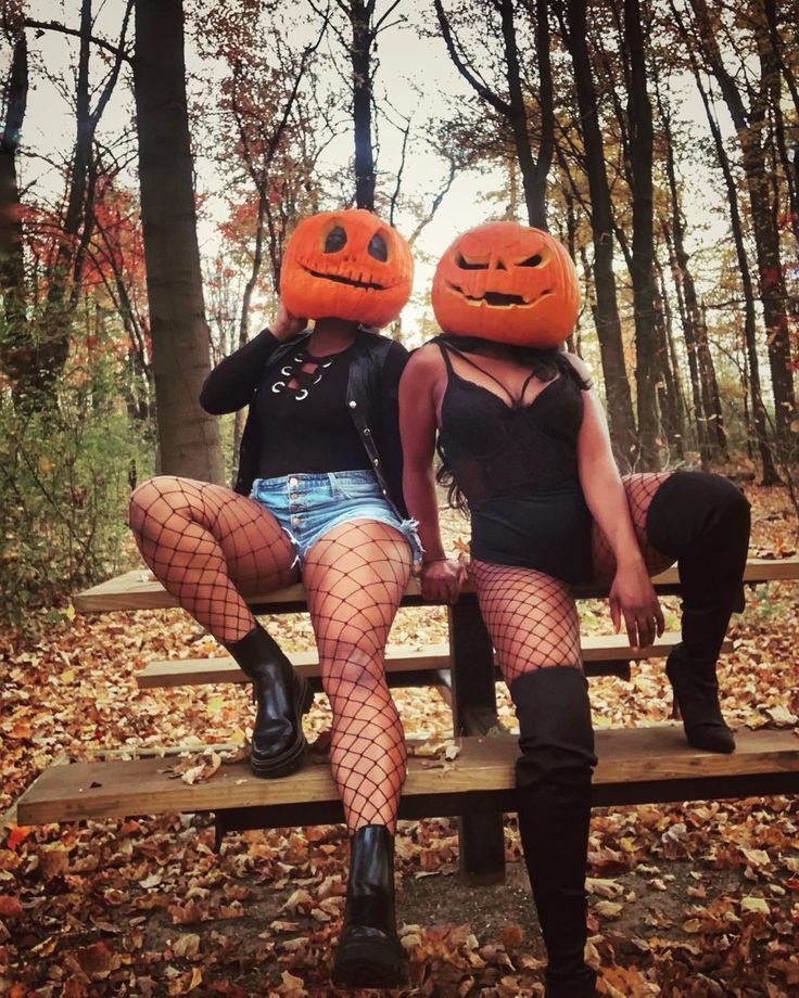 two women sitting on a bench with pumpkins on their heads and fish net stockings