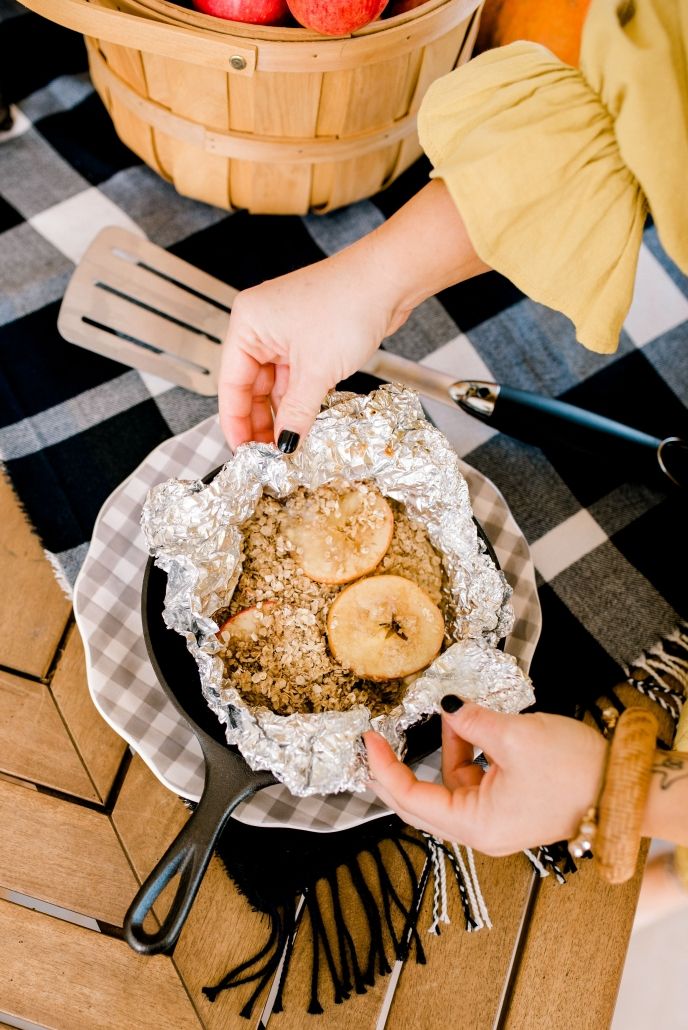 a person is holding an apple pie on a table with apples in the basket behind them