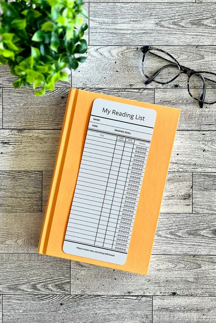 an orange book sitting on top of a wooden floor next to a pair of glasses