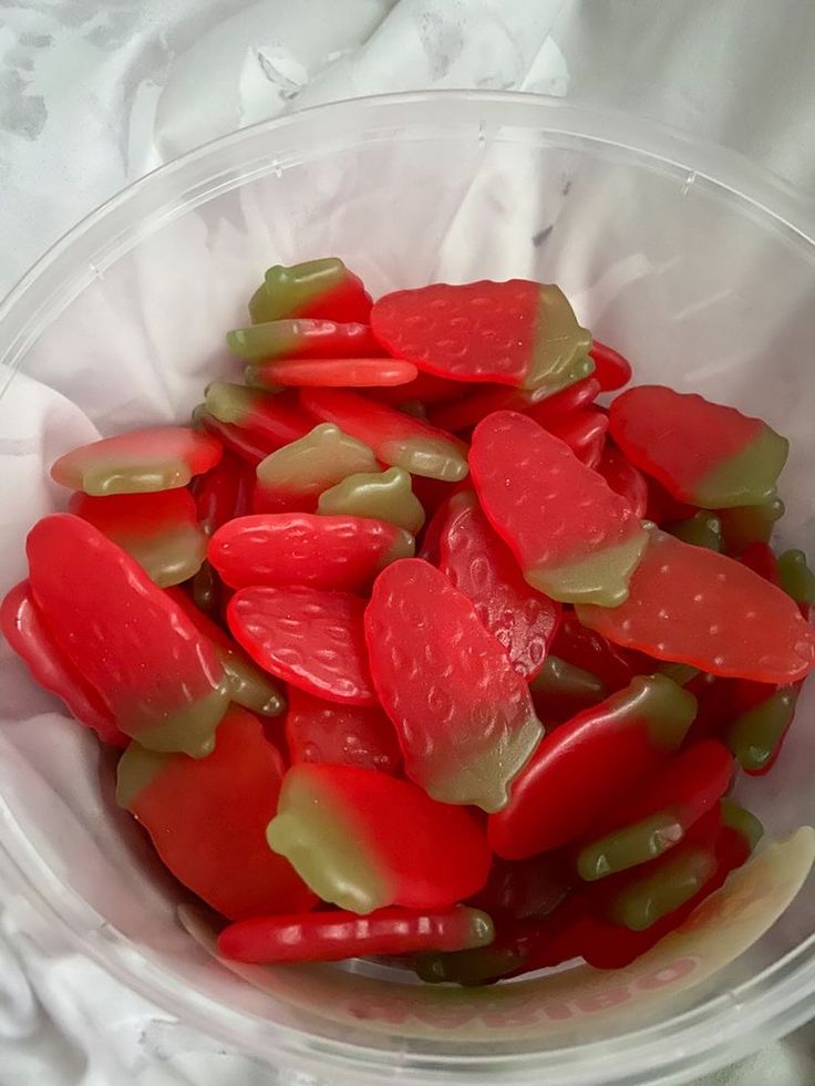 a bowl filled with red and green pickles on top of a white table cloth