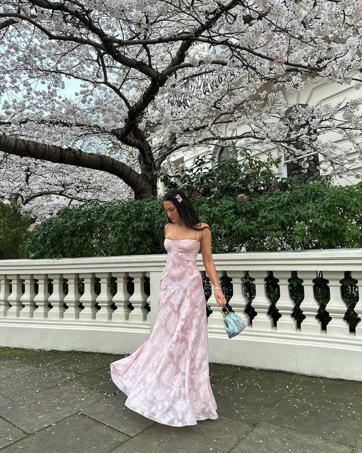 a woman in a pink dress is standing by a fence with cherry blossoms on it