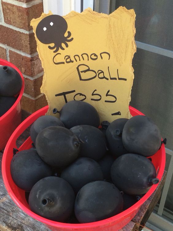 a red bucket filled with black plums next to a sign that says cannon ball toss