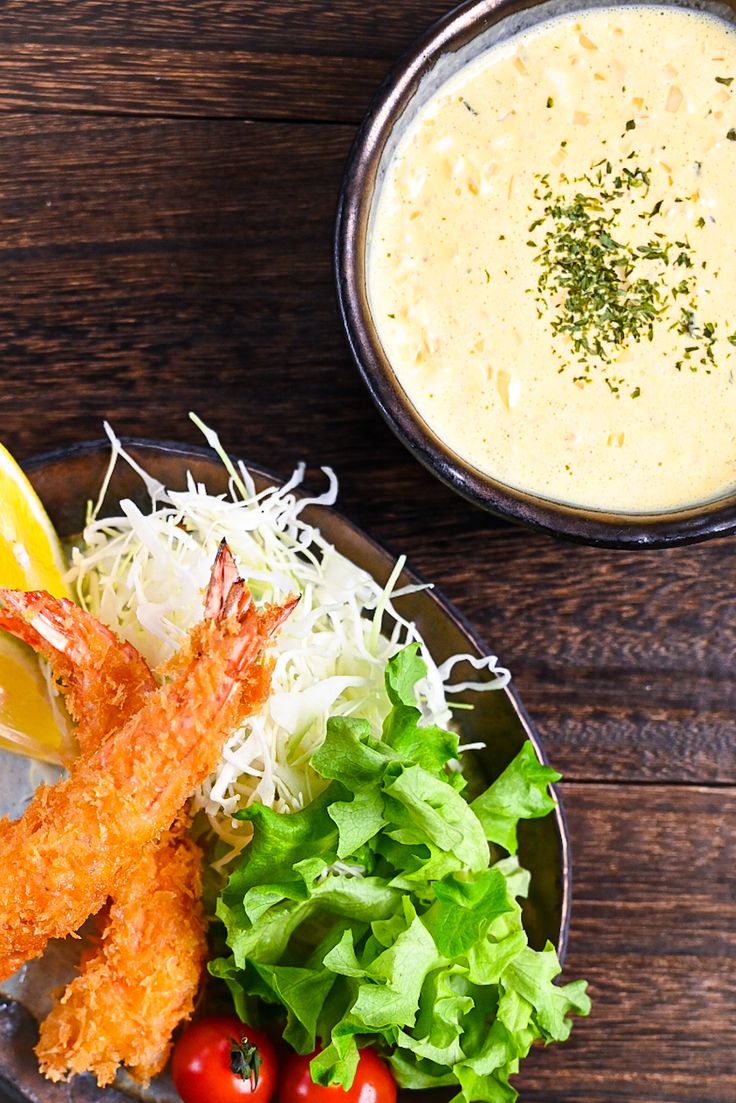 a plate with shrimp, lettuce and tomatoes next to a bowl of soup