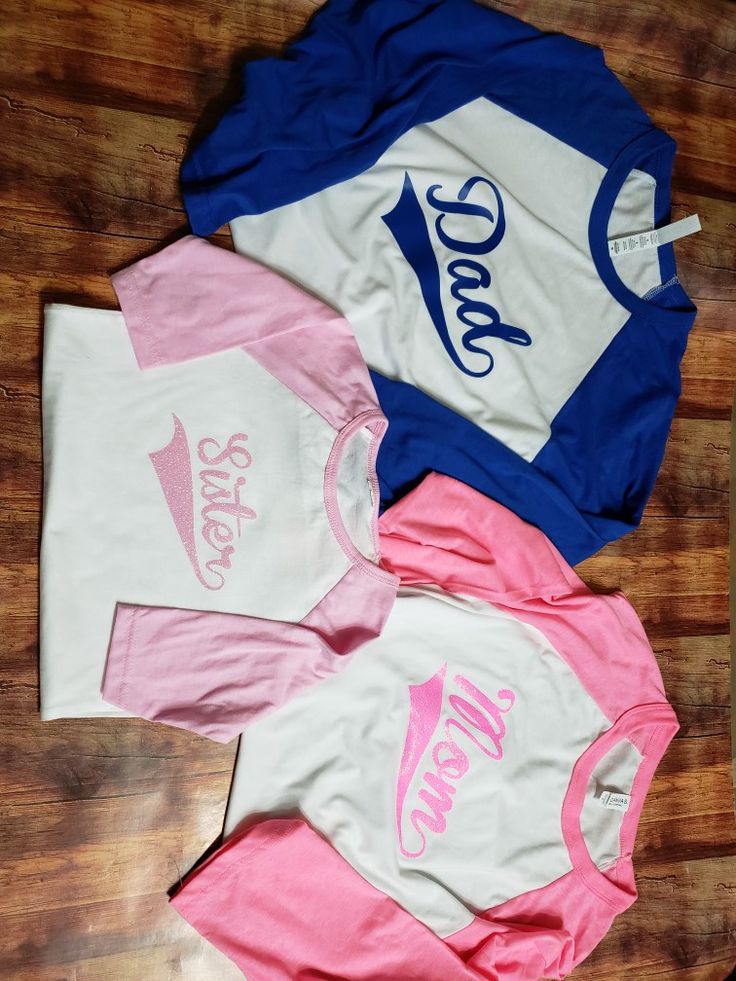 three different colored shirts sitting on top of a wooden floor next to each other with the word coca - cola printed on them