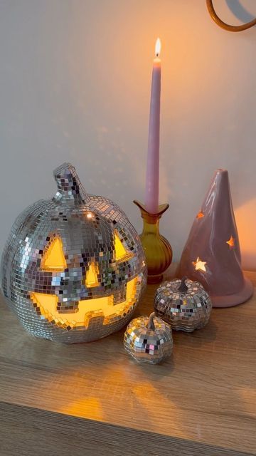 a lighted pumpkin sitting on top of a wooden table next to two silver balls and a candle