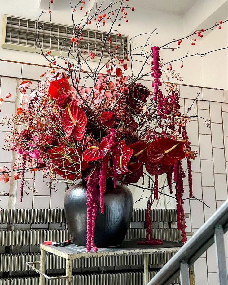 a vase filled with red flowers sitting on top of a wooden table next to a stair case