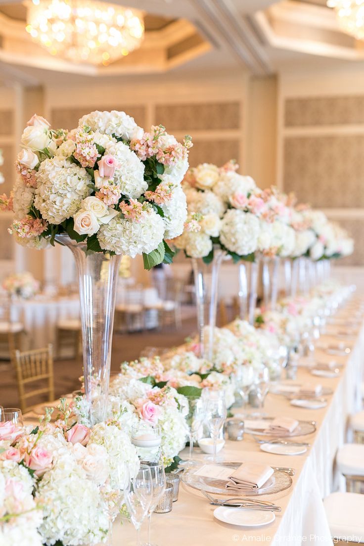 a long table with white and pink flowers in tall glass vases on each side