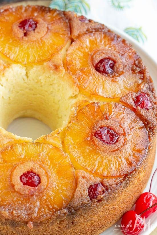 a pineapple upside down cake on a white plate with cherries around the edges