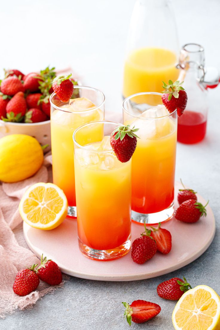 three glasses filled with orange juice and strawberries on a plate next to lemons