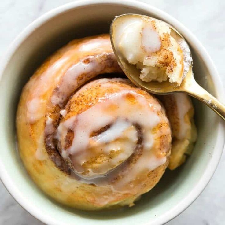 two cinnamon rolls in a white bowl with a spoon