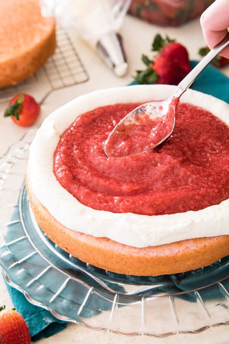 someone is spreading strawberry sauce on top of a cake with strawberries in the background