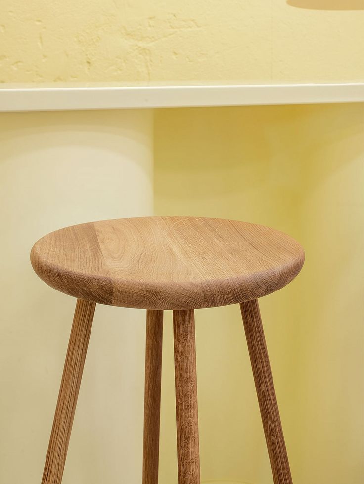 a wooden stool sitting on top of a hard wood floor next to a yellow wall