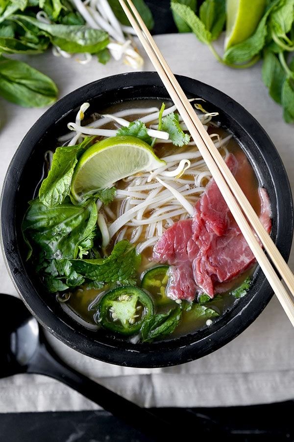 a black bowl filled with meat and veggies next to chopsticks