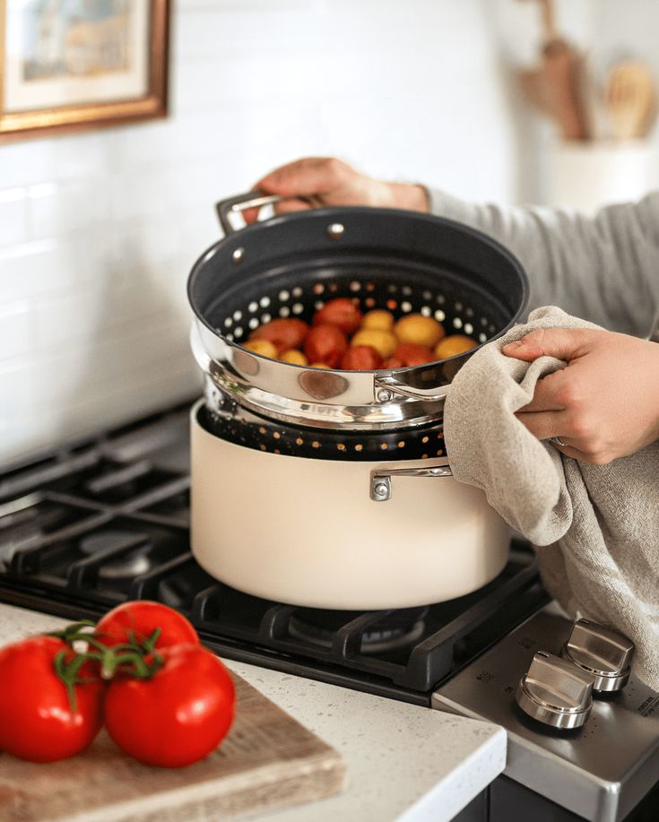 a woman is holding a cloth over the pot on the stove with tomatoes in it