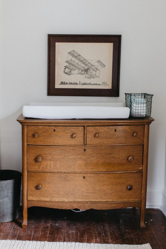 an old dresser with a baby's crib in front of it and a framed drawing on the wall